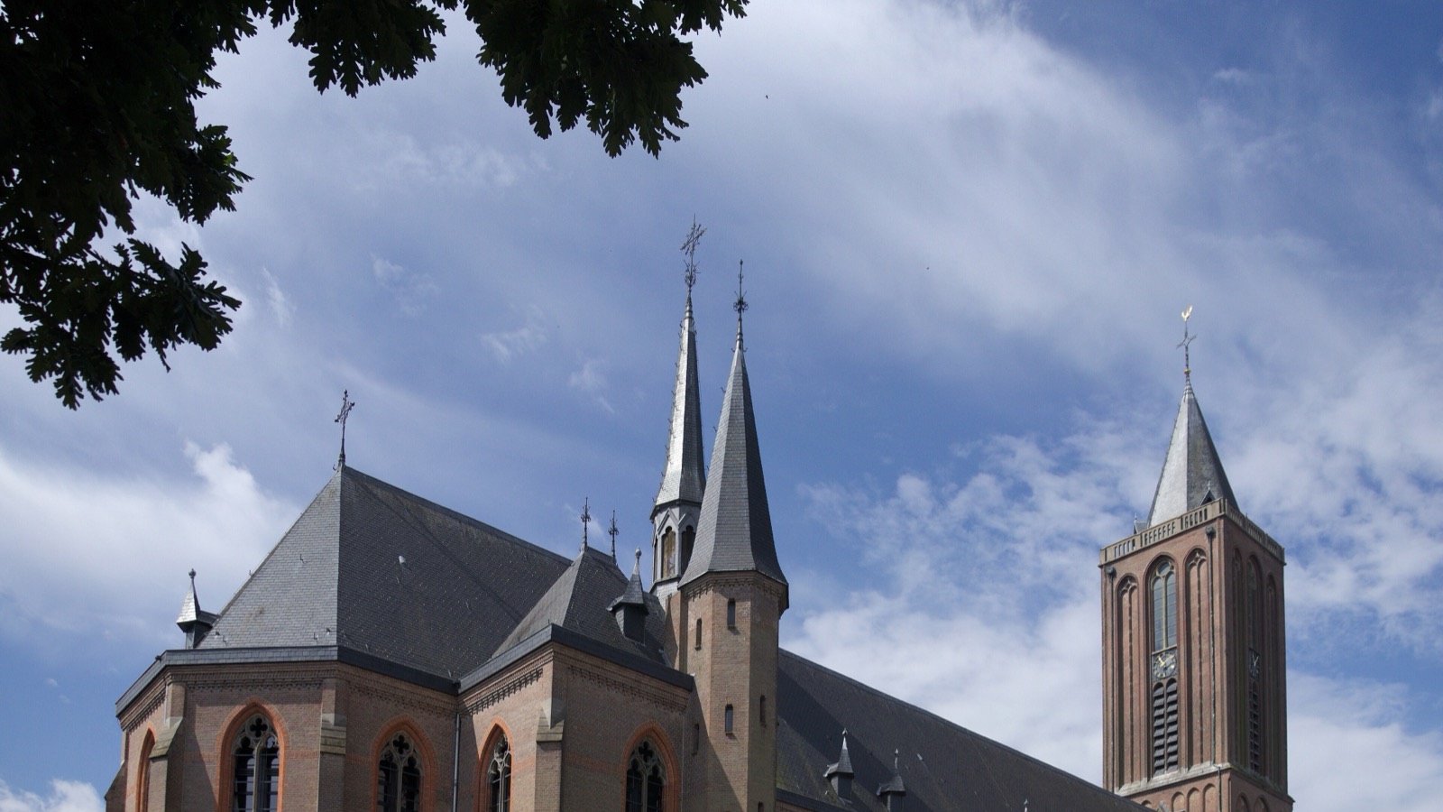 De voormalige Sint-Vituskerk in Bussum met haar torens tegen een blauwe lucht met wolken.