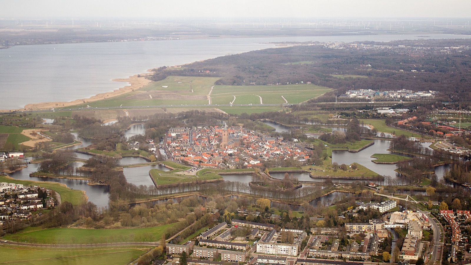 Luchtfoto van de stervormige vesting Naarden met haar grachten, de omliggende wijken en open water op de achtergrond.